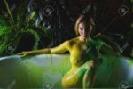 141271693-beautiful-woman-in-yellow-green-paint-on-a-background-of-indoor-plants-a-girl-with-very-large-takes.webp